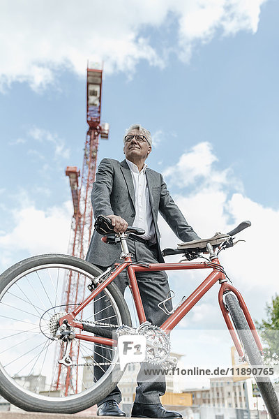 Portrait of senior businessman with bicycle in front of construction crane