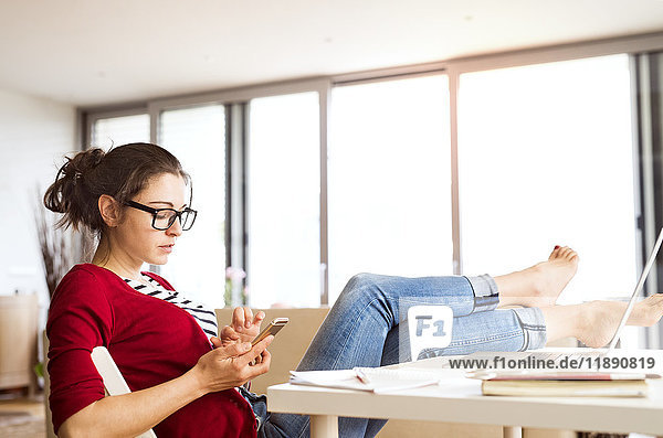 Frau sitzt zu Hause am Schreibtisch mit dem Smartphone