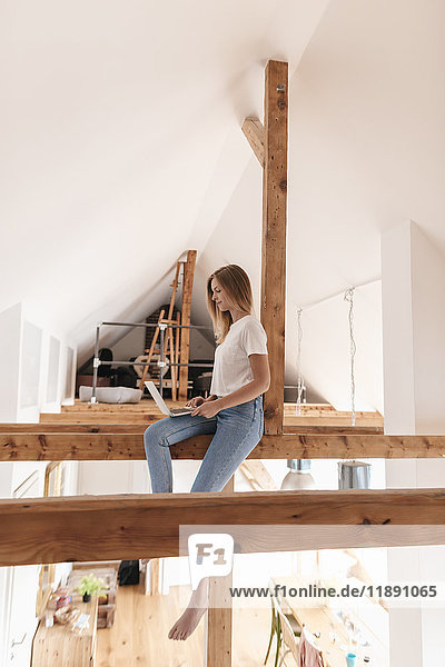 Carefree young woman sitting on ceiling joist  using laptop
