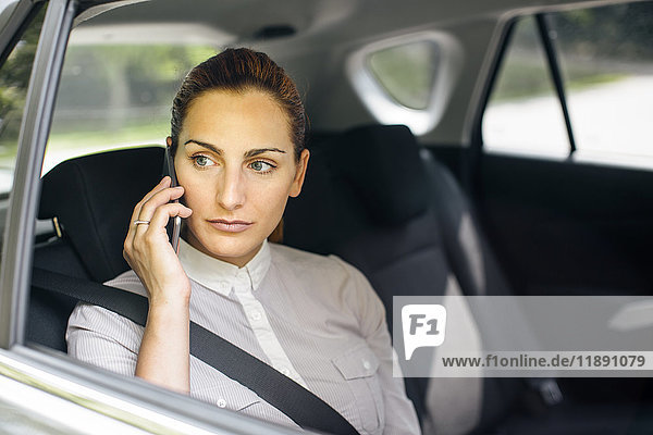 Geschäftsfrau am Telefon sitzend auf dem Rücksitz eines Autos