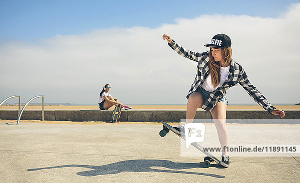 Young woman longboarding while her friend watching her