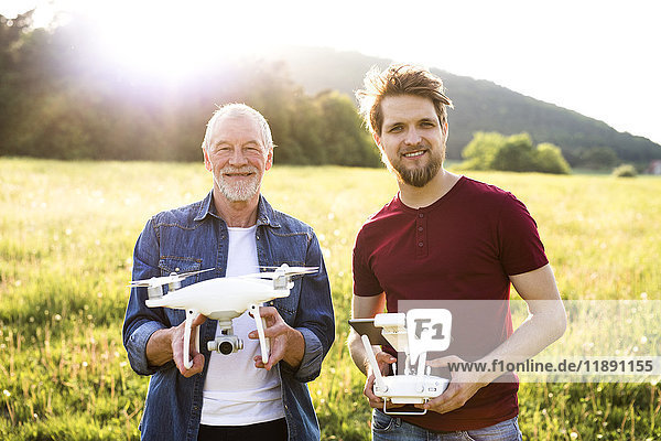Porträt des älteren Vaters und seines erwachsenen Sohnes mit Drohne auf einer Wiese
