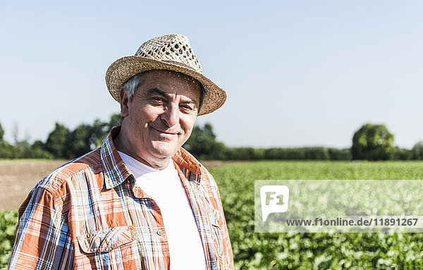 Portrait of content senior farmer standing in front of a field