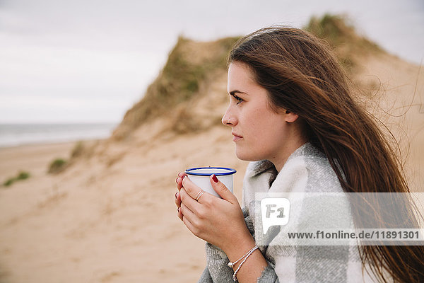 Junge Frau mit Tasse heißer Schokolade am Strand