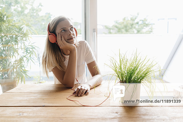 Junge Frau hört Musik mit Kopfhörern  die an Topfpflanzen angeschlossen sind.