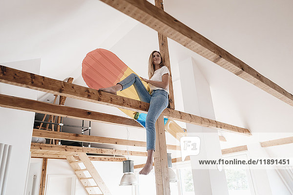 Carefree young woman sitting on ceiling joist  holding colorful airbed