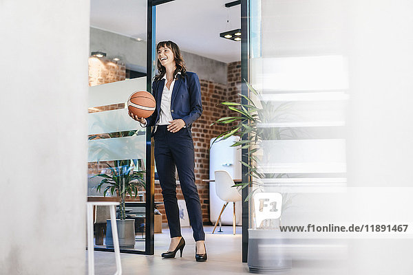 Businesswoman holding basket ball in office