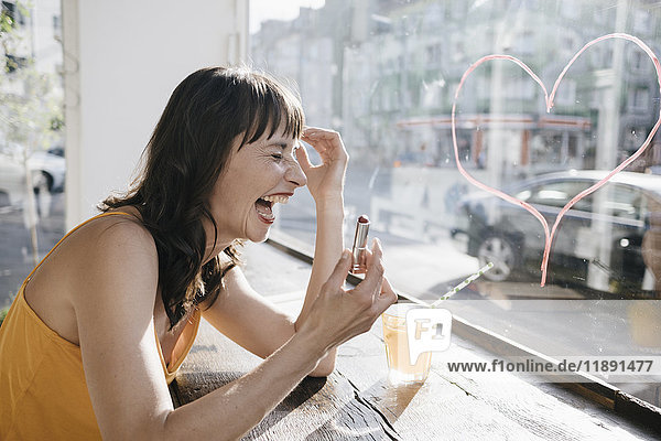 Frau im Café sitzend zeichnet Herzform auf Fensterscheibe mit Lippenstift