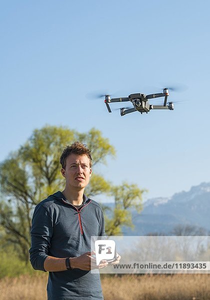 Junger Mann steuert fliegenden Quadrocopter  ferngesteuerte Drohne mit Kamera  DJI Mavic