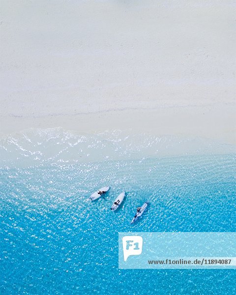 High Angle View of Three People Relaxing auf Paddle Boards auf blauem Wasser