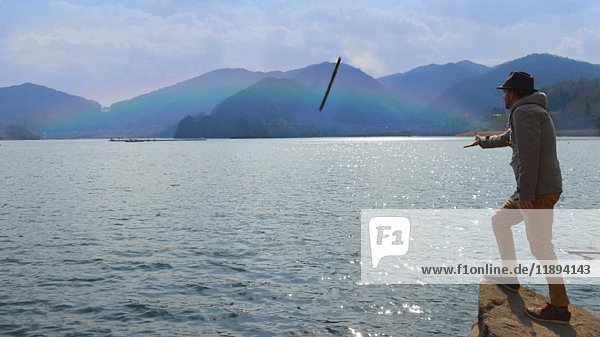 Man Throwing Stick at Rainbow at Edge of Lake