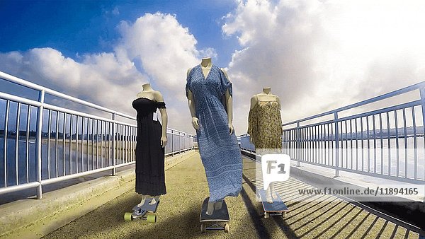 Drei weibliche Schaufensterpuppen fahren auf Skateboards entlang des Stegs  während ihre Kleider im Wind wehen