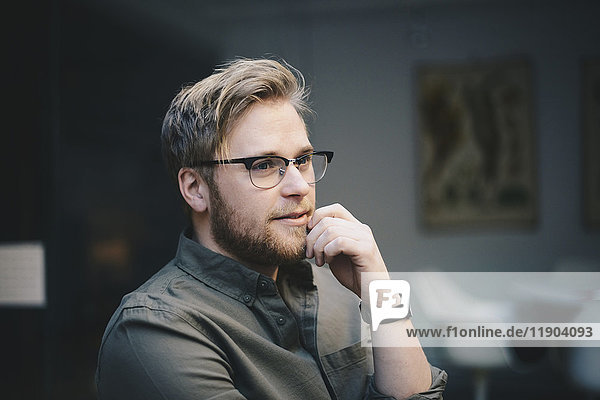 Thoughtful male computer programmer with hand on chin looking away in office