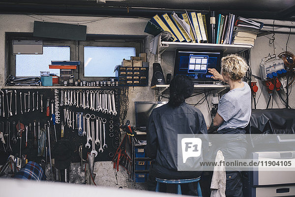 Mechanikerinnen diskutieren über Computermonitor in der Autowerkstatt
