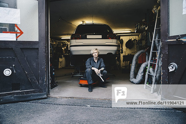 Mechanikerin sitzend mit dem Auto am Eingang der Autowerkstatt