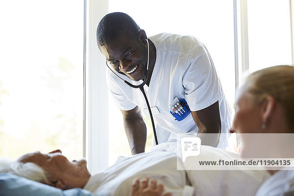 Glückliche Krankenschwestern im Gespräch mit einem älteren Mann  der auf dem Bett in der Krankenstation liegt.