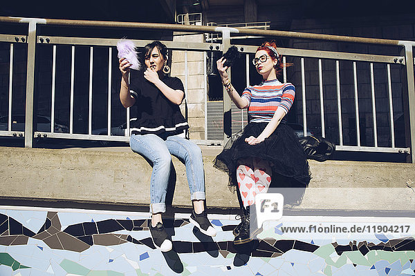 Hipster-Freundinnen nehmen Selfie mit dem Handy  während sie an der Wand gegen das Geländer sitzen.