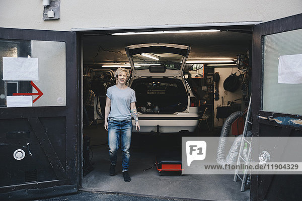Full length portrait of happy owner at entrance of auto repair shop