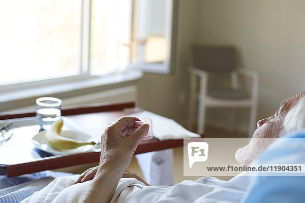 Senior man taking cough syrup while reclining on hospital bed