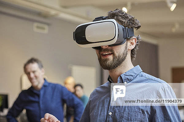 Männlicher Profi mit Virtual-Reality-Simulator gegen Kollegen im Kreativbüro