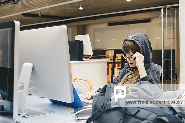 Weibliche Programmiererin mit Laptop beim Blick über die Brille im Büro