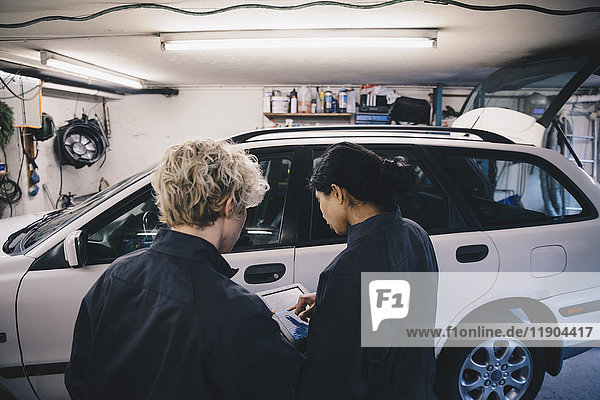 Female mechanic explaining coworker over digital tablet in auto repair shop
