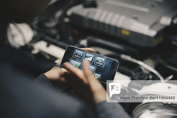 Beschnittenes Bild des Mechanikers mit Anwendung auf dem Smartphone bei geöffnetem Auto