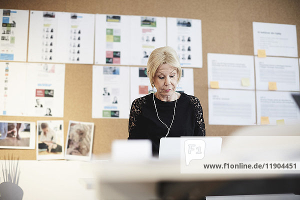Senior Geschäftsfrau mit Kopfhörer gegen das Schwarze Brett im Kreativbüro