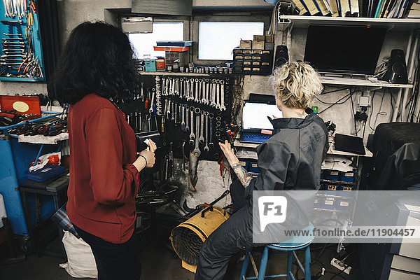 Mechanikerin erklärt Kunde über Laptop in der Autowerkstatt