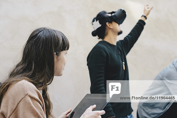 Männliche Computerprogrammierer  die mit einer VR-Brille von Kollegen im Büro gestikulieren.