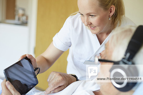 Lächelnde Krankenschwester mit digitalem Tablett und älterem Mann auf der Krankenstation