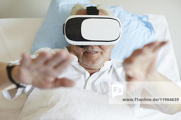 Großer Blickwinkel auf die Gestik des älteren Mannes bei der Verwendung einer VR-Brille auf dem Bett in der Krankenstation.