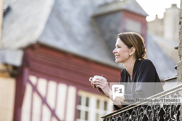 Kaukasische Frau trinkt Kaffee auf einem Balkon in der Stadt