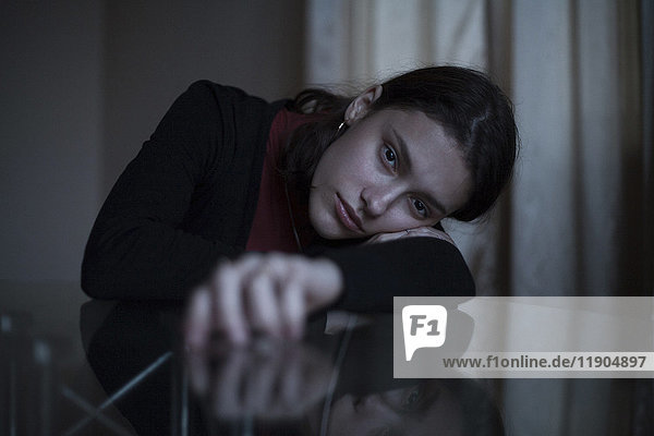 Porträt einer ernsten kaukasischen Frau  die sich mit dem Gesicht auf den Arm am Tisch stützt