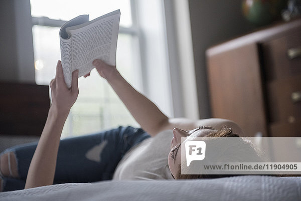 Kaukasische Frau liegt auf dem Bett und liest ein Buch