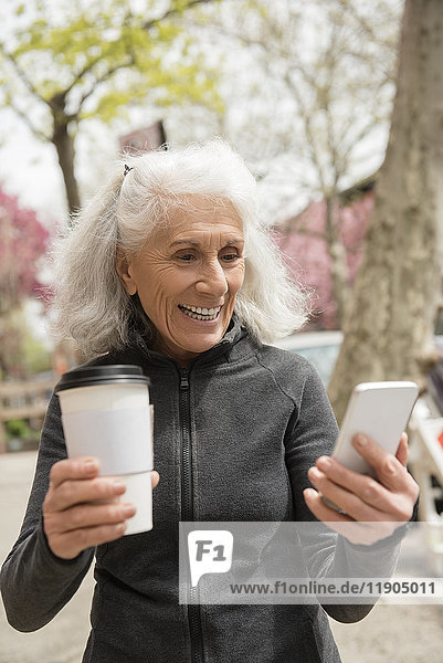 Ältere Frau trinkt Kaffee und schreibt eine SMS mit ihrem Handy