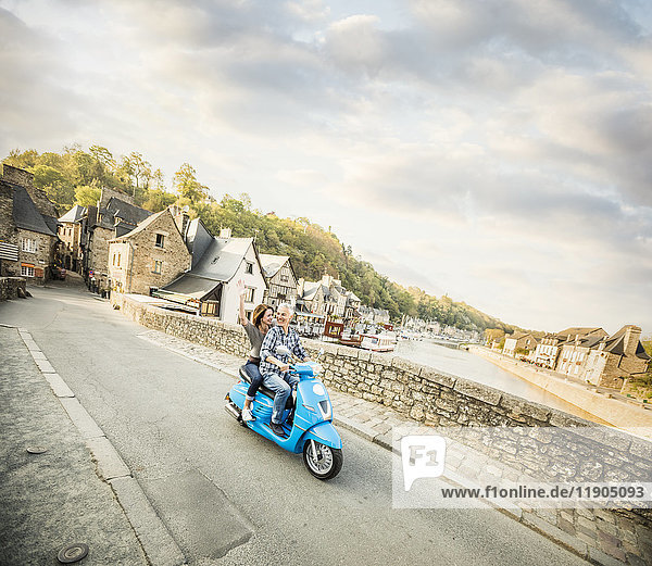 Unbekümmertes kaukasisches Paar fährt blauen Motorroller in der Nähe des Flusses