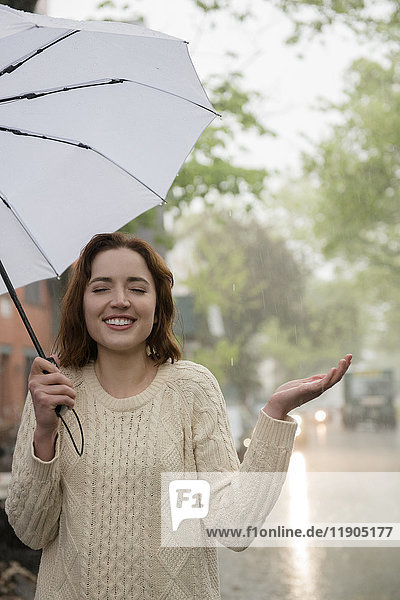 Sorglose kaukasische Frau hält Regenschirm im Regen