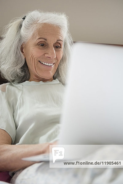 Ältere Frau liegt im Bett und benutzt einen Laptop