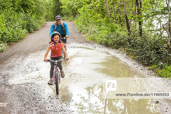 Father and daughter riding bicycles through puddle