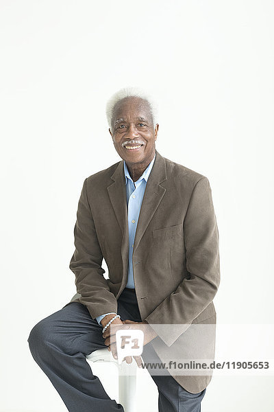 Porträt eines älteren lächelnden schwarzen Mannes  der auf einem Hocker sitzt