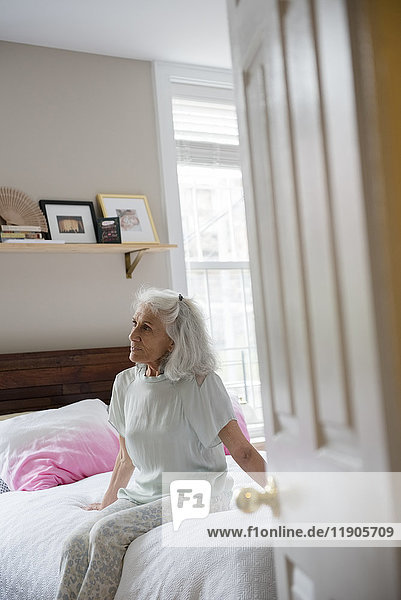 Ältere Frau sitzt auf dem Bett jenseits der Eingangstür