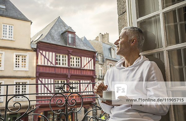 Kaukasischer Mann rührt auf einem Balkon in der Stadt Kaffee um