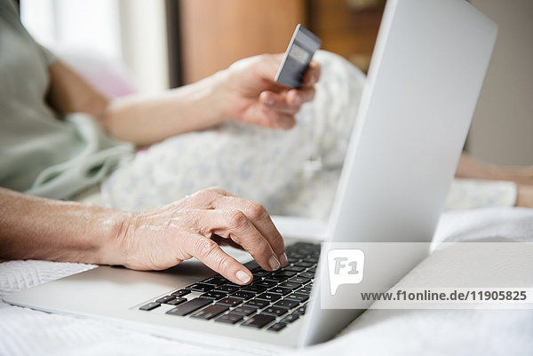 Hände einer älteren Frau beim Online-Shopping mit Kreditkarte und Laptop