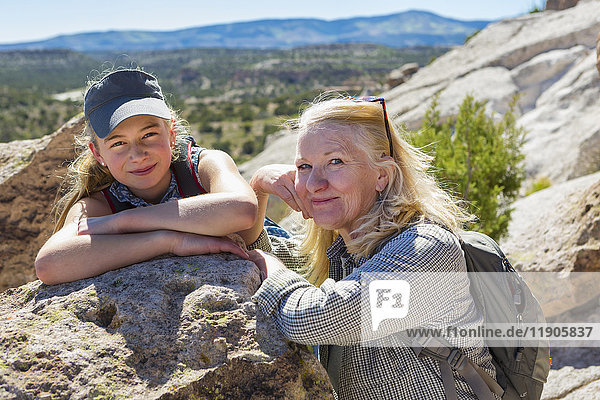Porträt einer kaukasischen Großmutter und einer Enkelin  die sich an einen Felsen lehnen