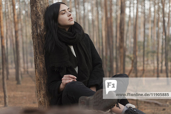 Nachdenkliche kaukasische Frau sitzt auf einem Baumstamm im Wald