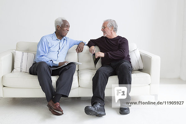 Ältere Männer lesen auf dem Sofa sitzend Zeitschriften