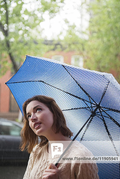 Kaukasische Frau hält Regenschirm und schaut nach oben
