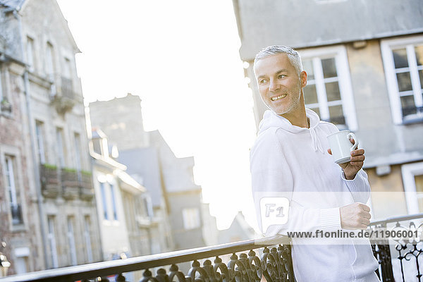 Kaukasischer Mann trinkt Kaffee auf dem Balkon in der Stadt