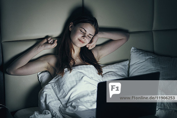 Fatigued Caucasian woman using laptop in bed